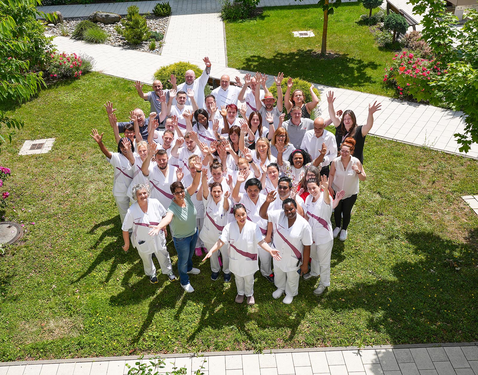 Das Foto zeigt eine Gruppe von Mitarbeiterinnen und Mitarbeitern des Maria Stadler Haus. Es wurde von einer erhöhten Position aufgenommen. Die Personen auf dem Foto winken in die Kamera.