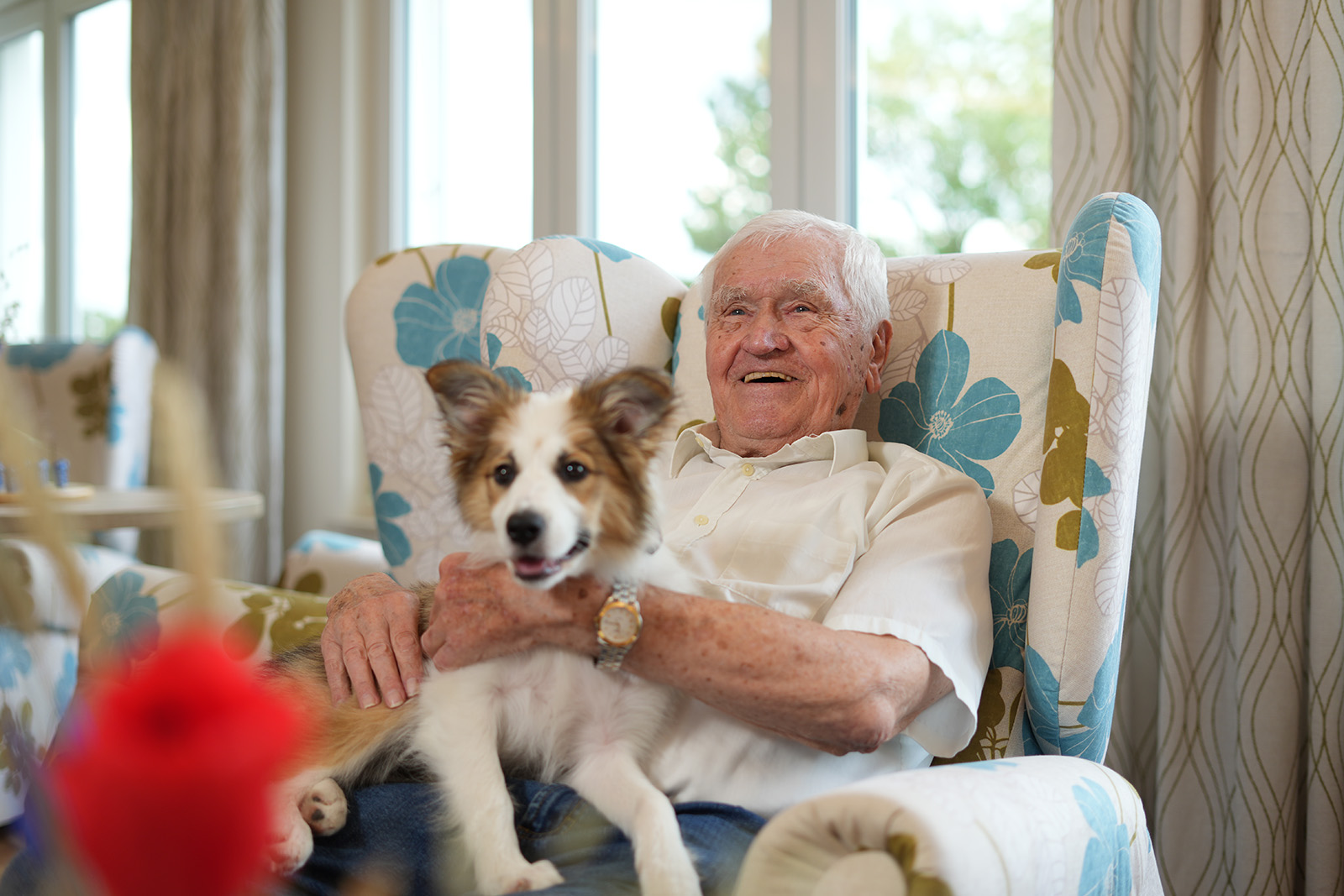 Das Foto zeigt einen Bewohner des Maria Stadler Haus mit seinem Hund auf einem Sessel sitzend.